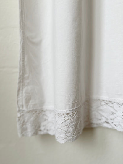 White lace hem detail of a dress hanging on a plain background