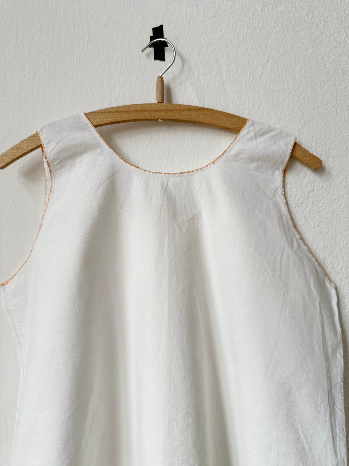 Back detail of a white sleeveless vintage dress on a wooden hanger against a white wall