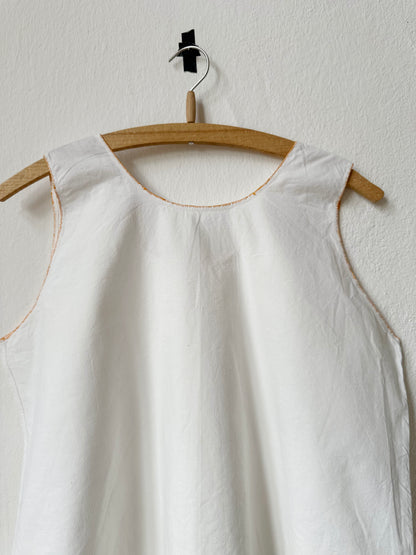 Back detail of a white sleeveless vintage dress on a wooden hanger against a white wall
