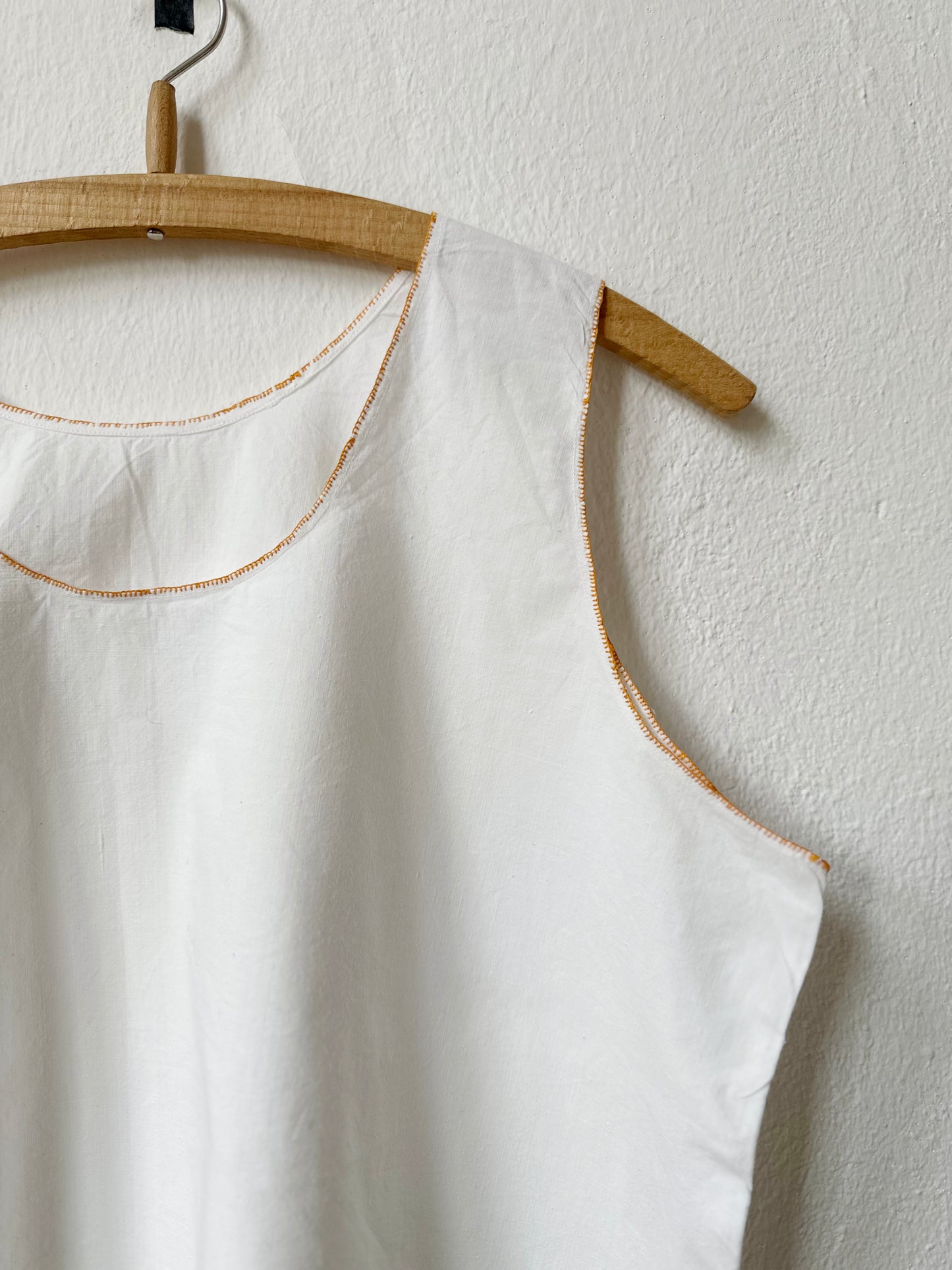 Detail of white sleeveless vintage dress on a wooden hanger against a light gray wall