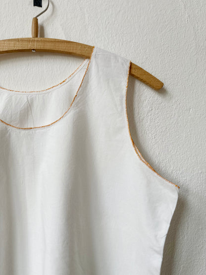 Detail of white sleeveless vintage dress on a wooden hanger against a light gray wall