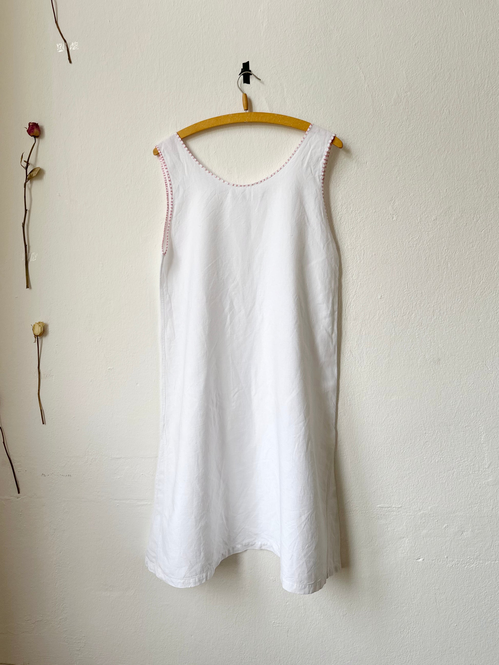 White sleeveless vintage dress hanging on a wooden hanger against a plain white wall.