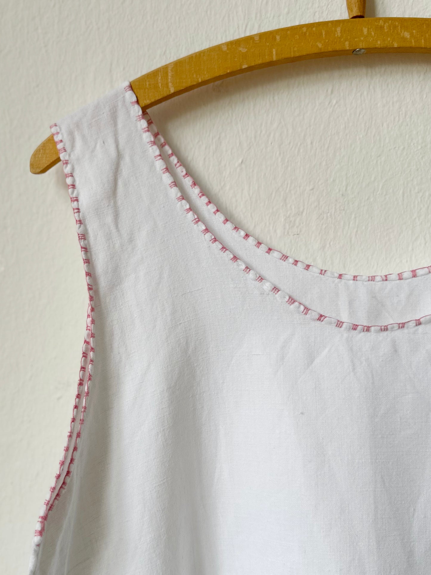 White sleeveless top with pink trim on a wooden hanger against a white background