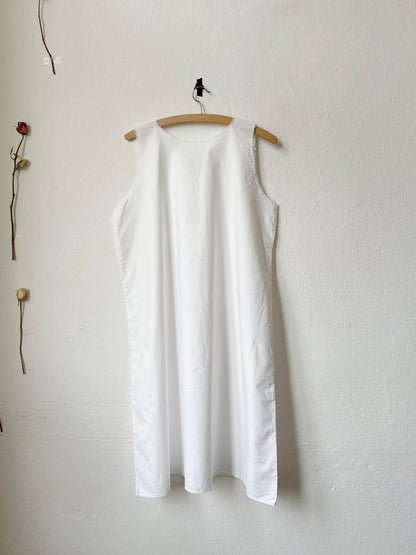 White sleeveless vintage dress hanging on a wooden hanger against a white wall.