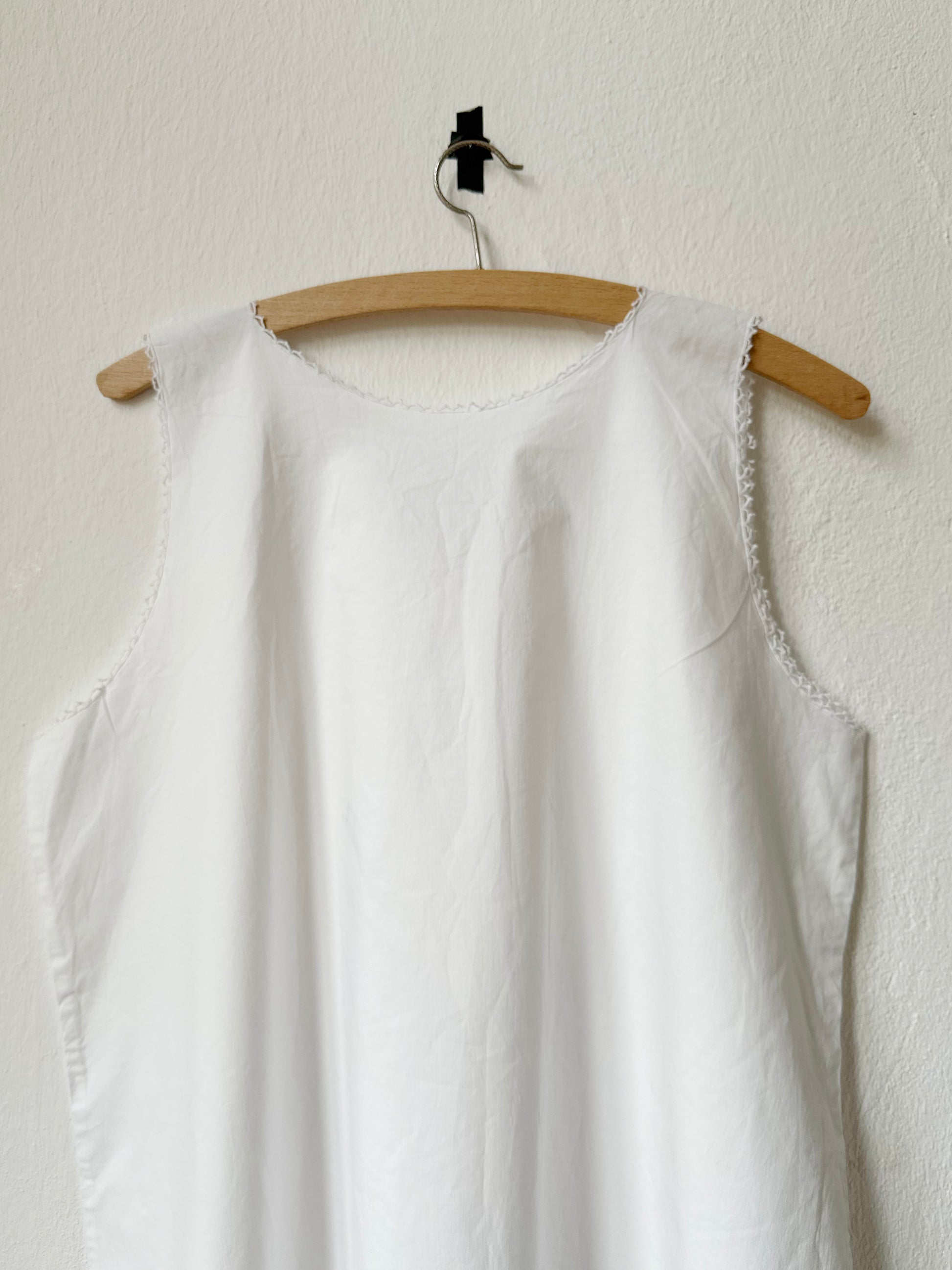 White vintage sleeveless dress on a wooden hanger against a white wall