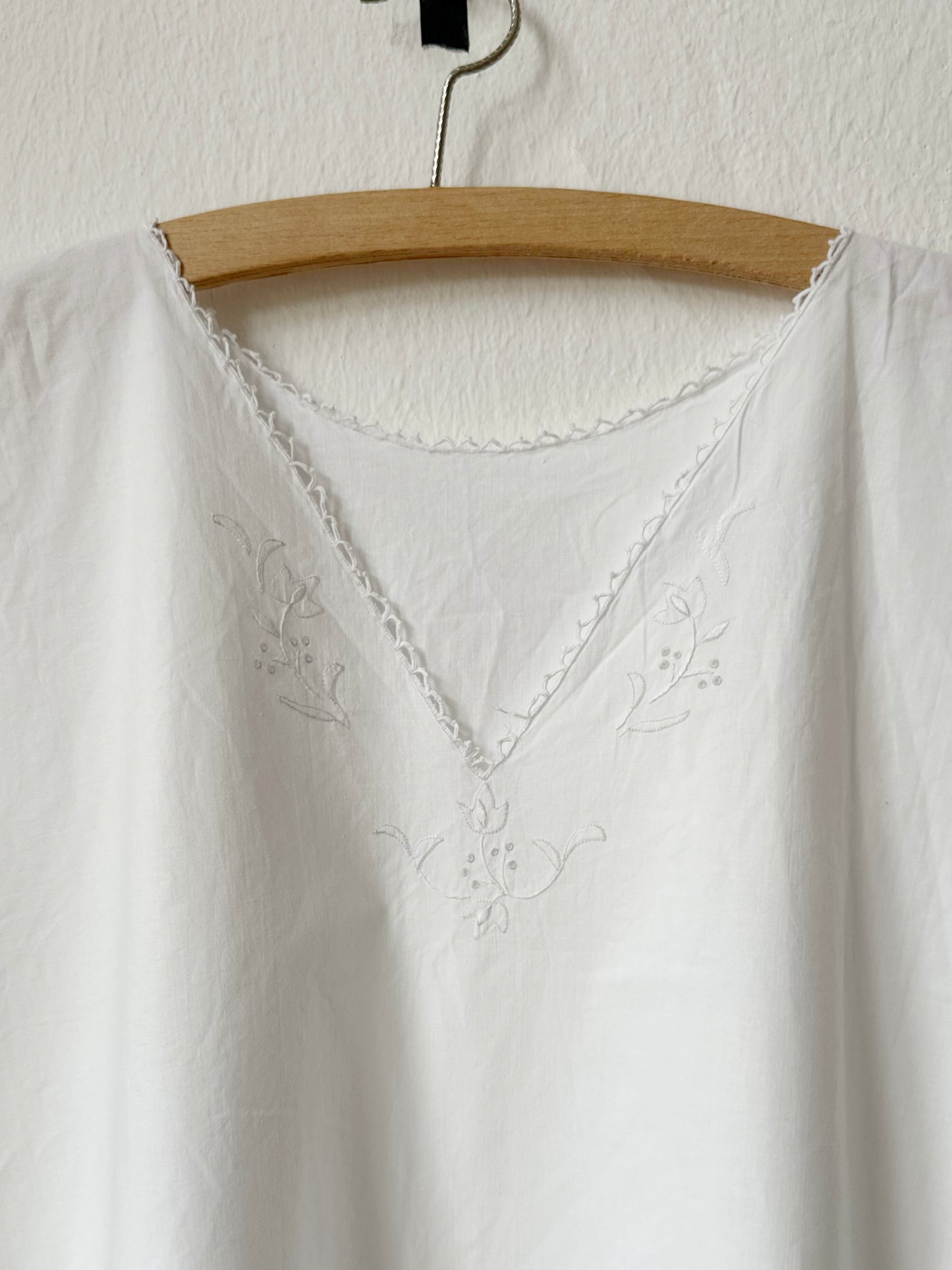 Vintage white embroidered dress on a wooden hanger against a white background