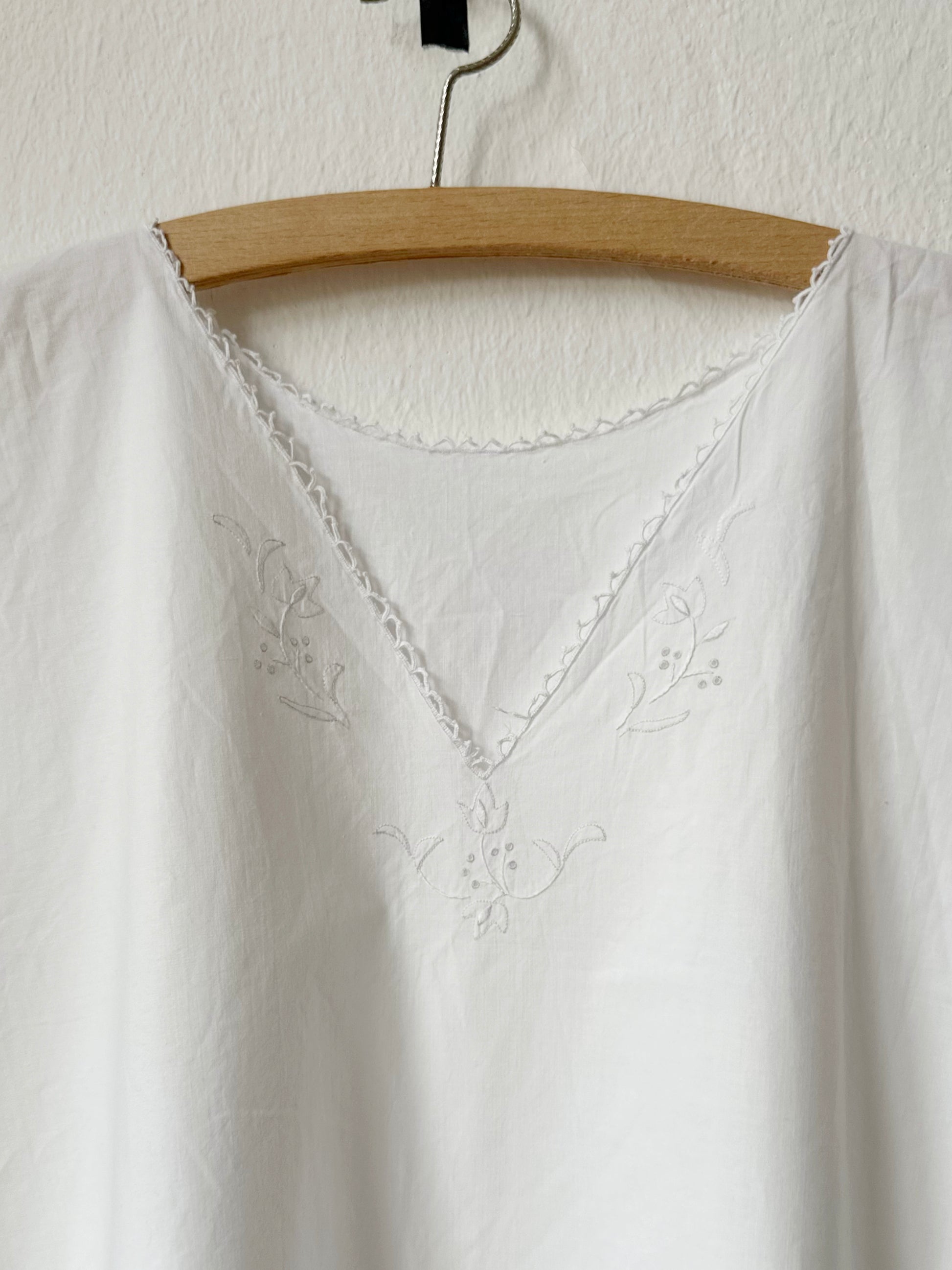 Vintage white embroidered dress on a wooden hanger against a white background