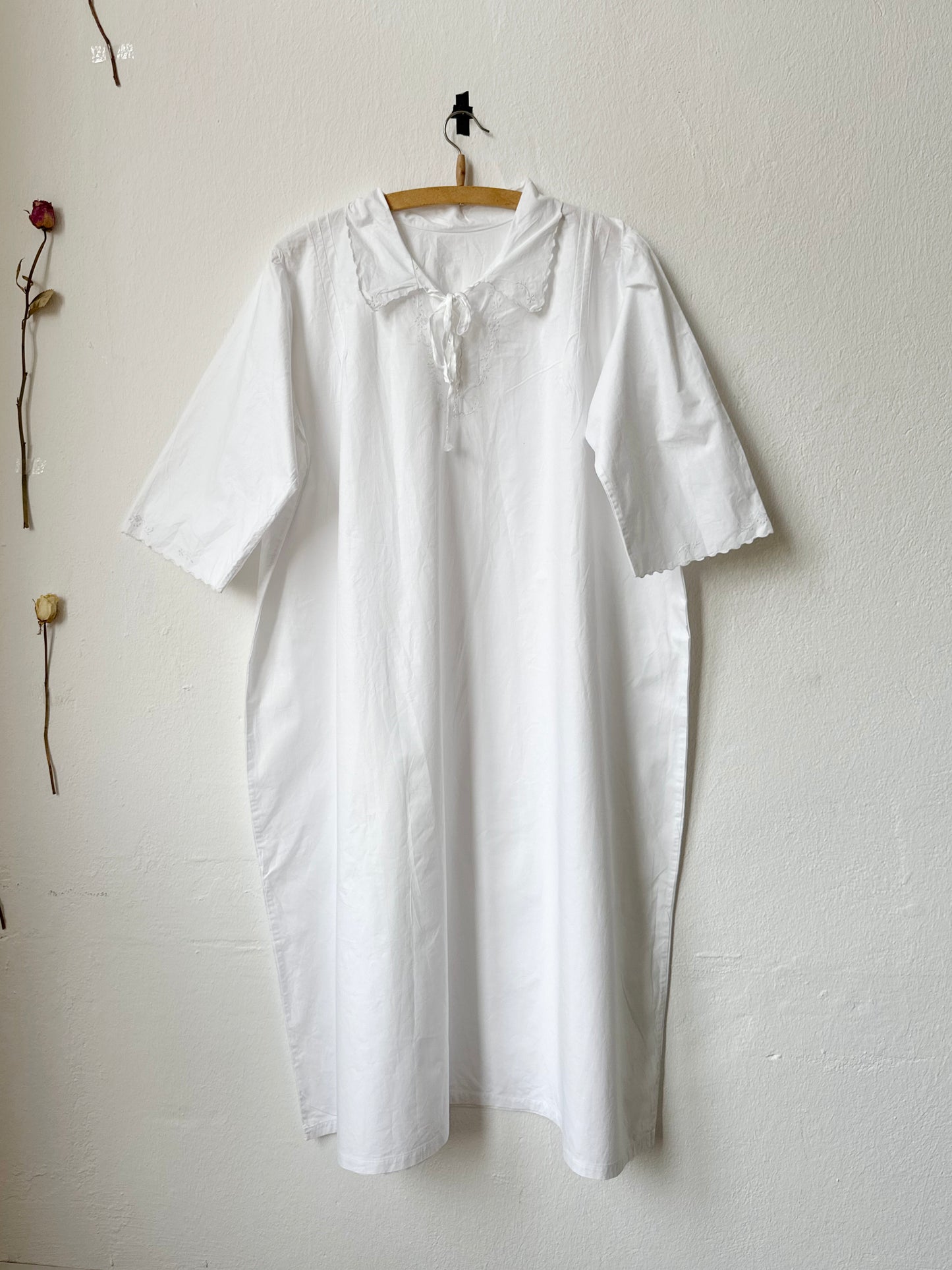 White vintage dress hanging on a wooden hanger against a plain white wall.