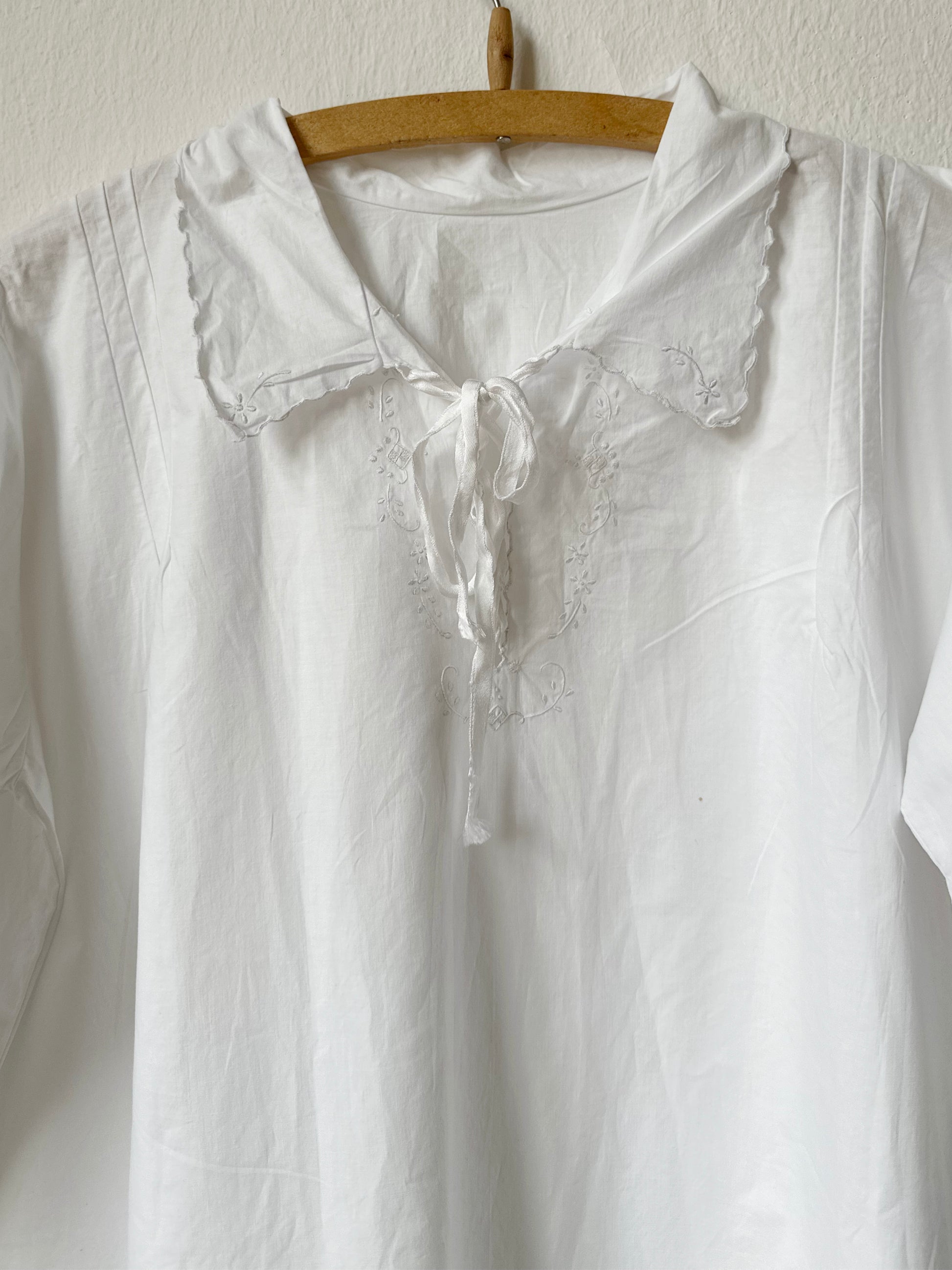 White dress with lace details on a wooden hanger against a white background