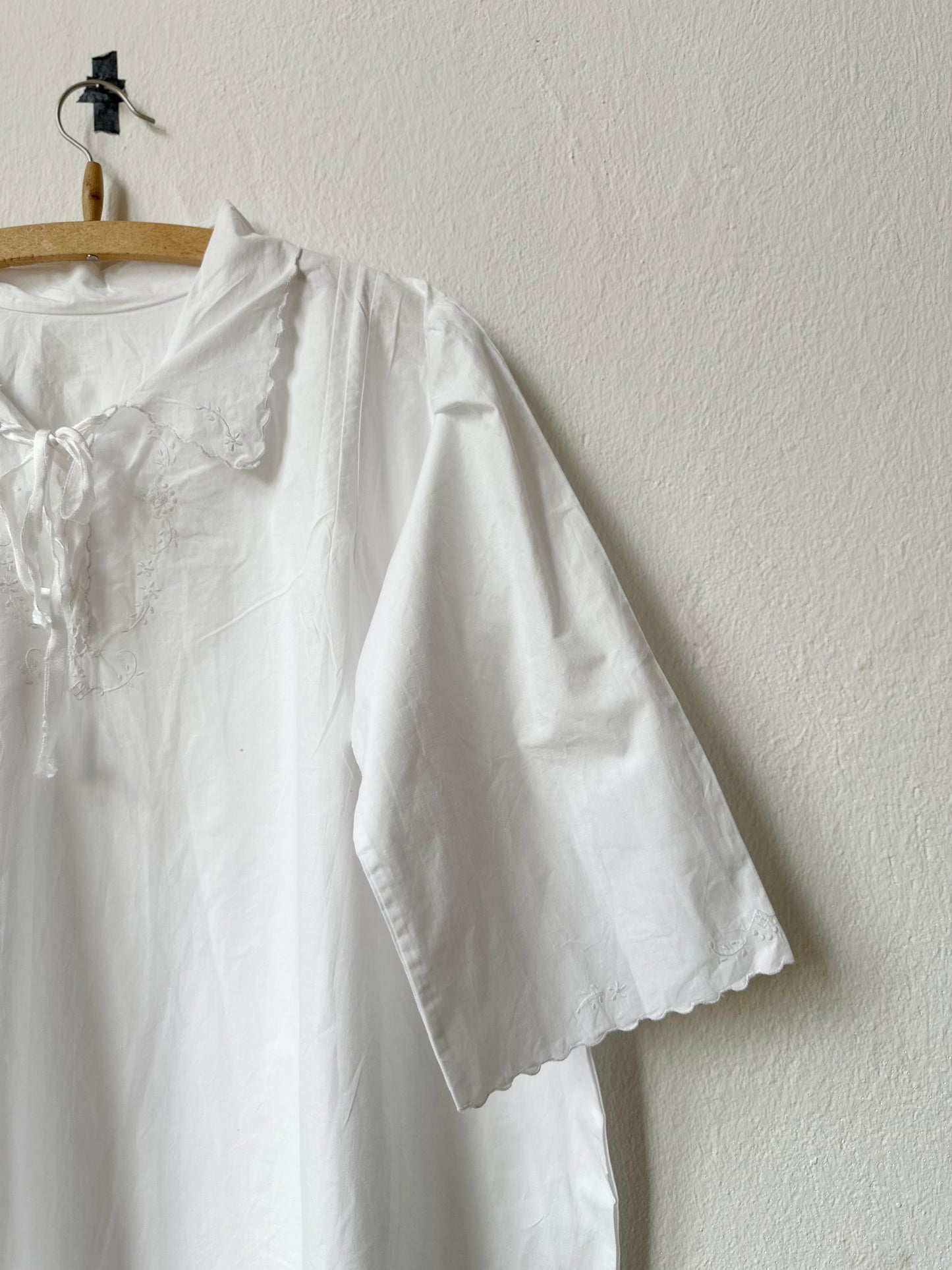 Sleeve detail of a white dress with lace details hanging on a wooden hanger against a plain wall.