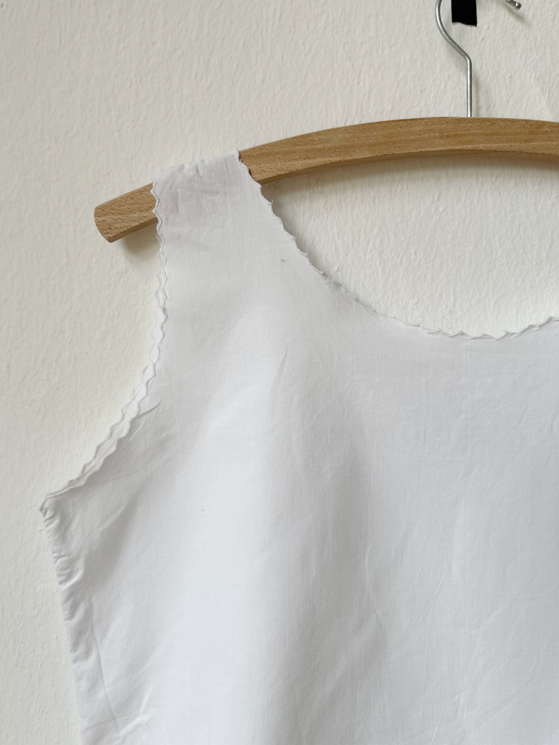 White sleeveless top on a wooden hanger against a white wall