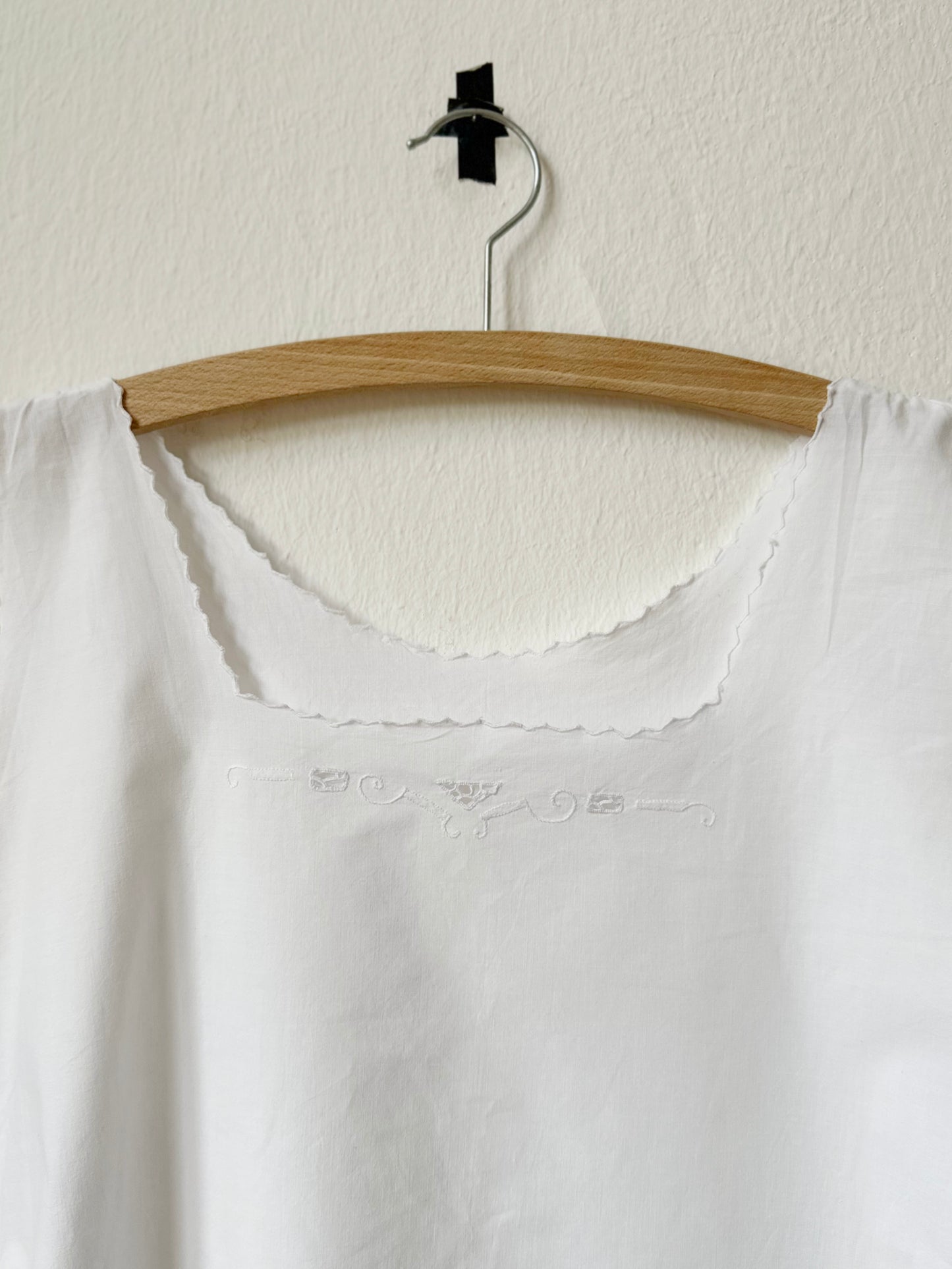 Vintage white blouse on a wooden hanger against a white wall