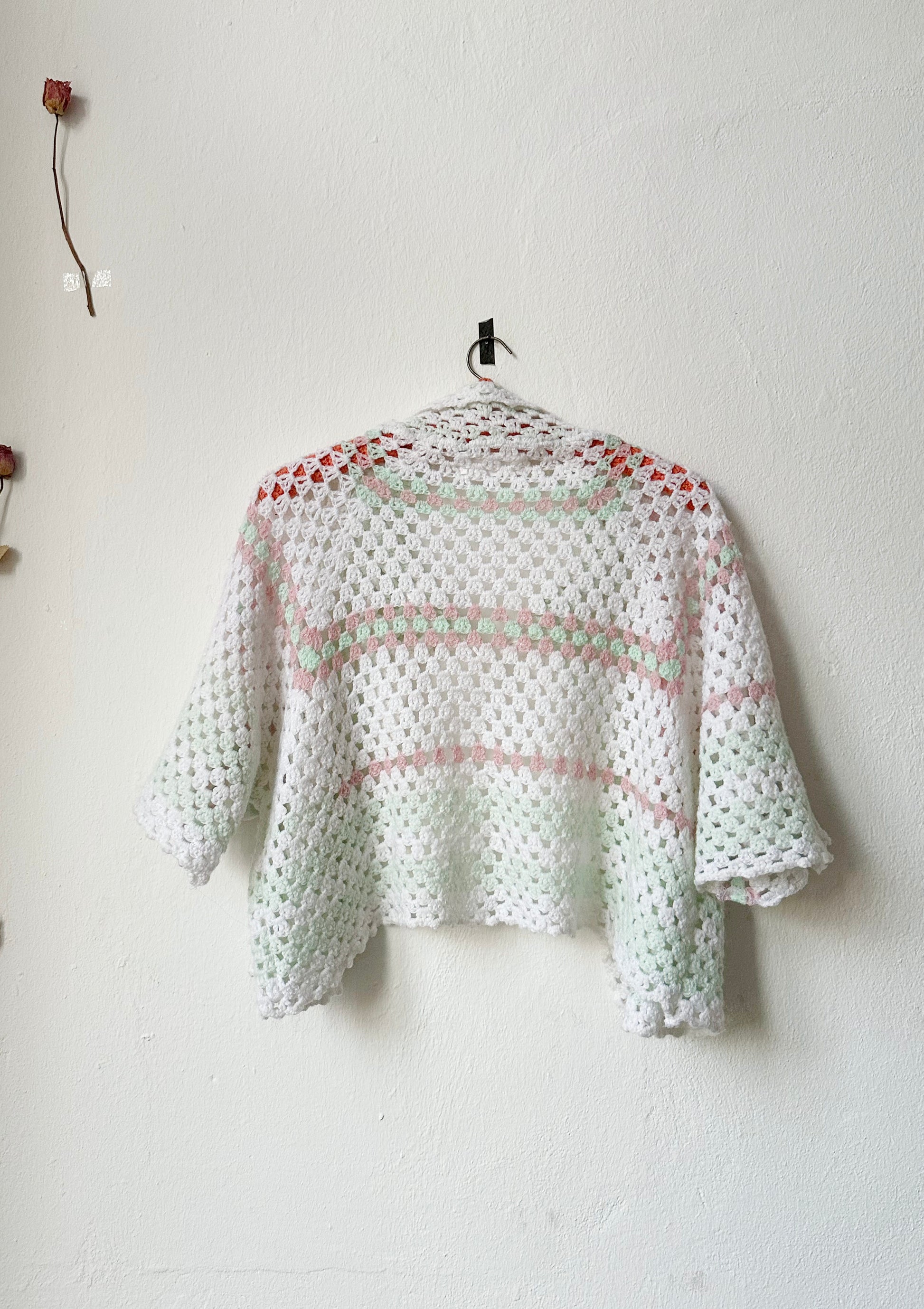 A back view of the stripe crochet jacket hanging on a wall.