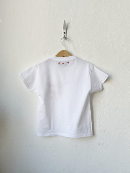 White t-shirt with small red hearts on a hanger against a white wall