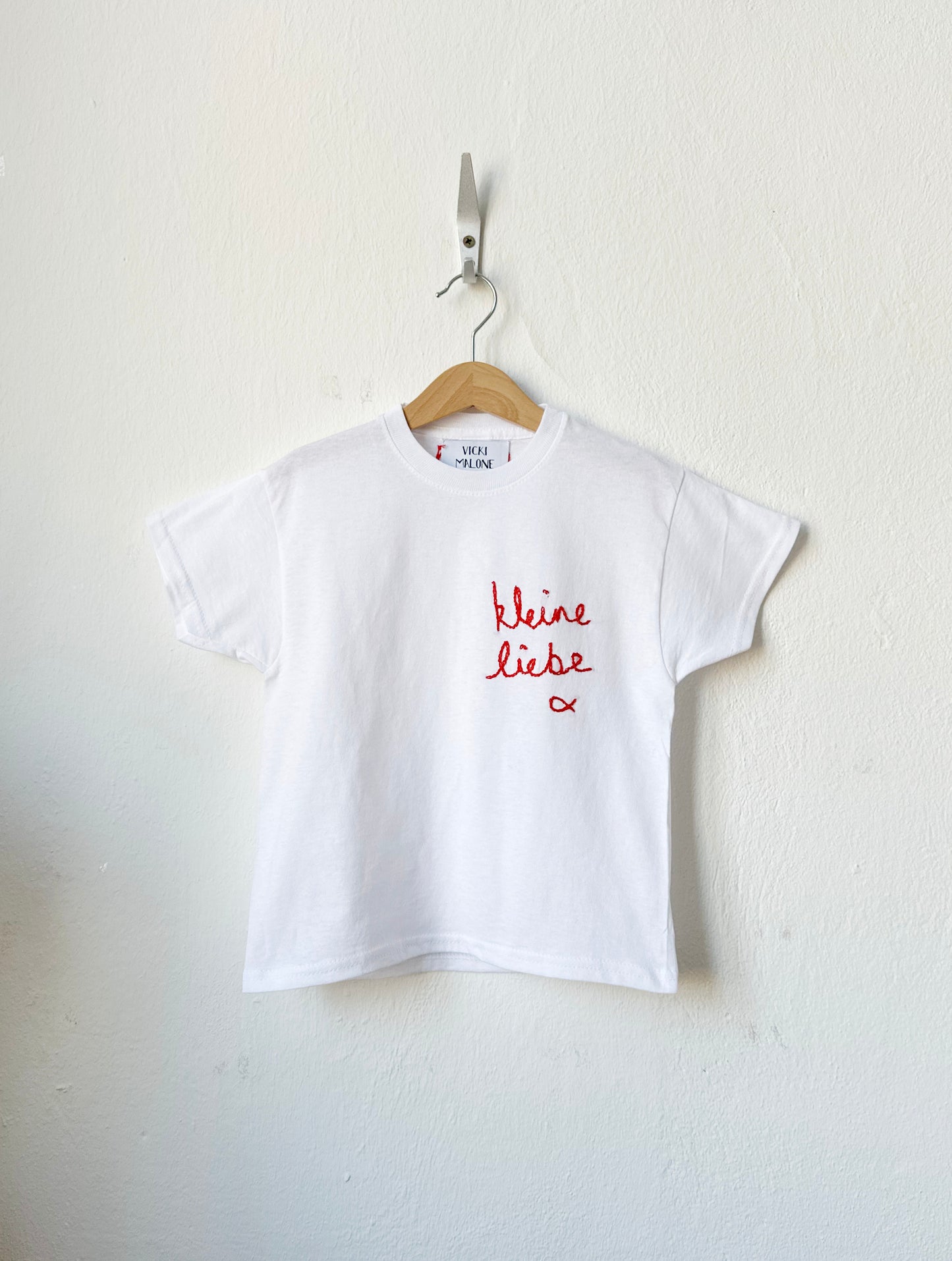 White t-shirt with red text on a hanger against a white background
