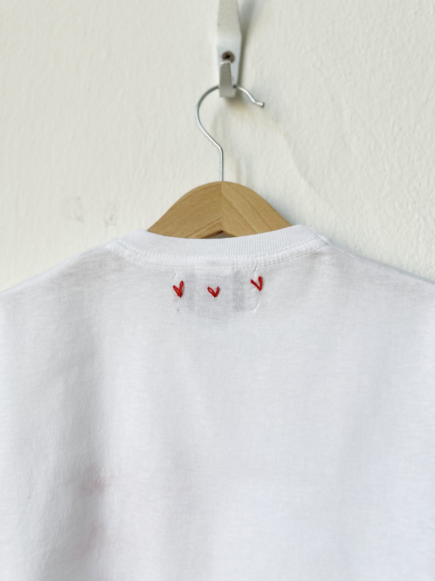 White shirt with red embroidery on a wooden hanger against a white background