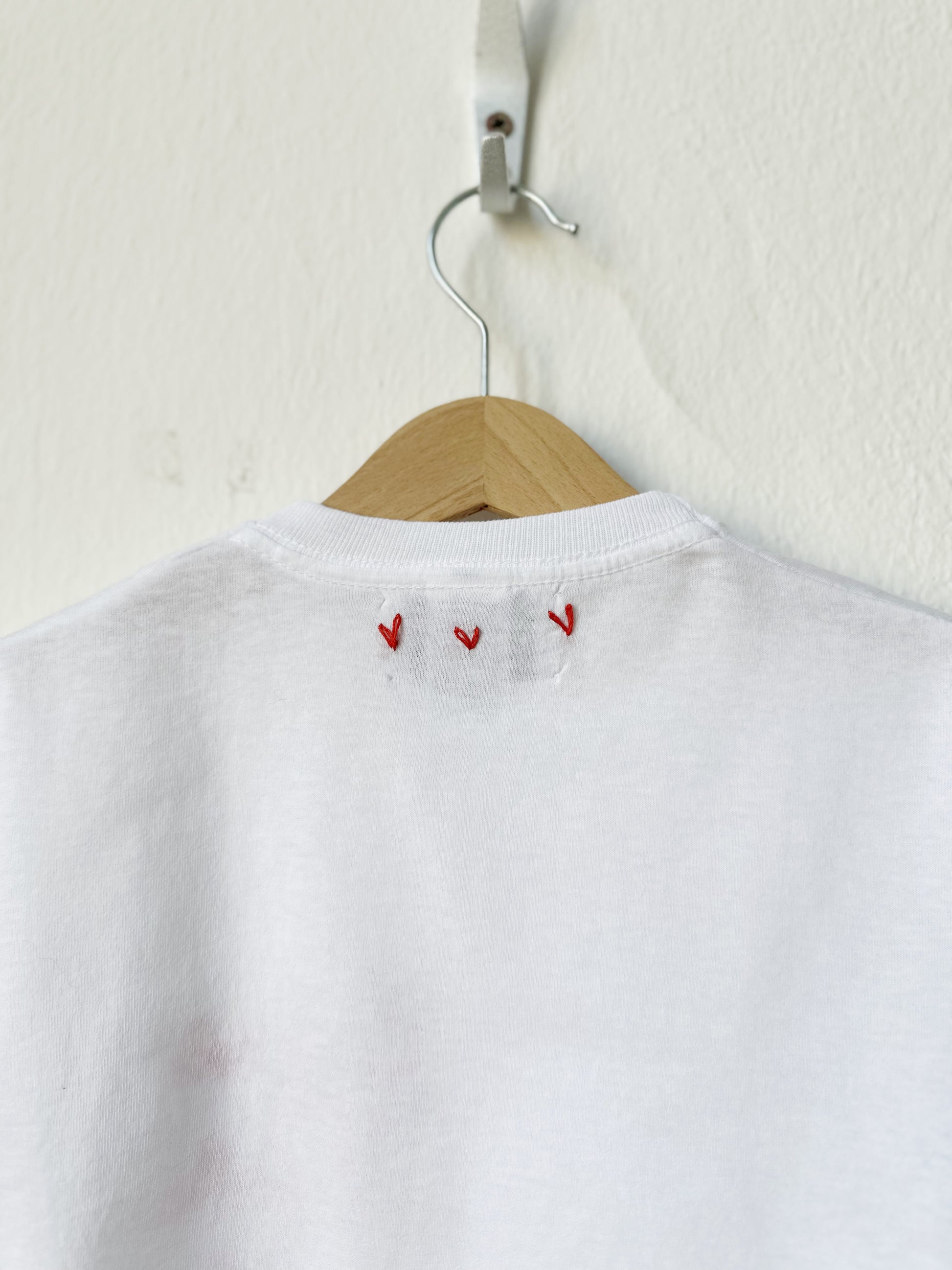 White shirt with red embroidery on a wooden hanger against a white background